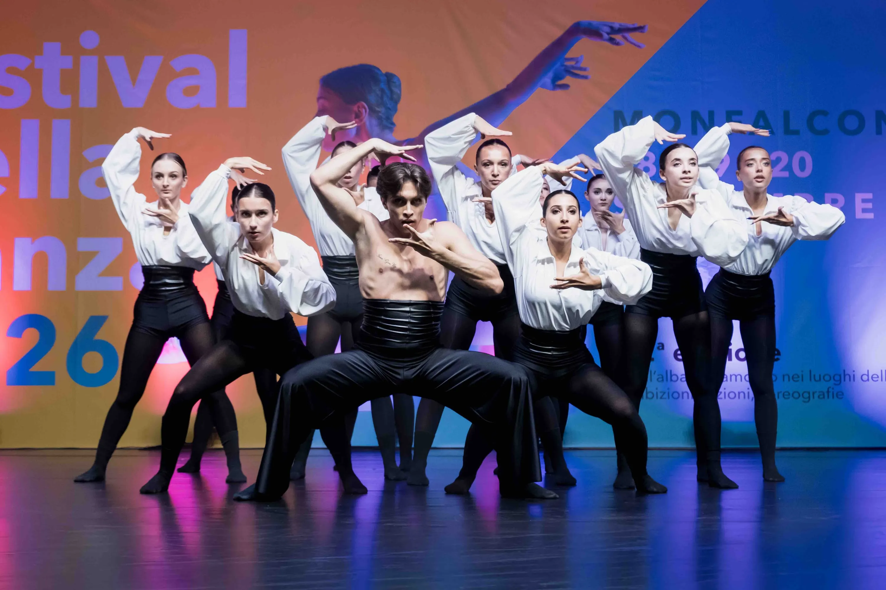 A group of dancers in white shirts posing before the festival backdrop