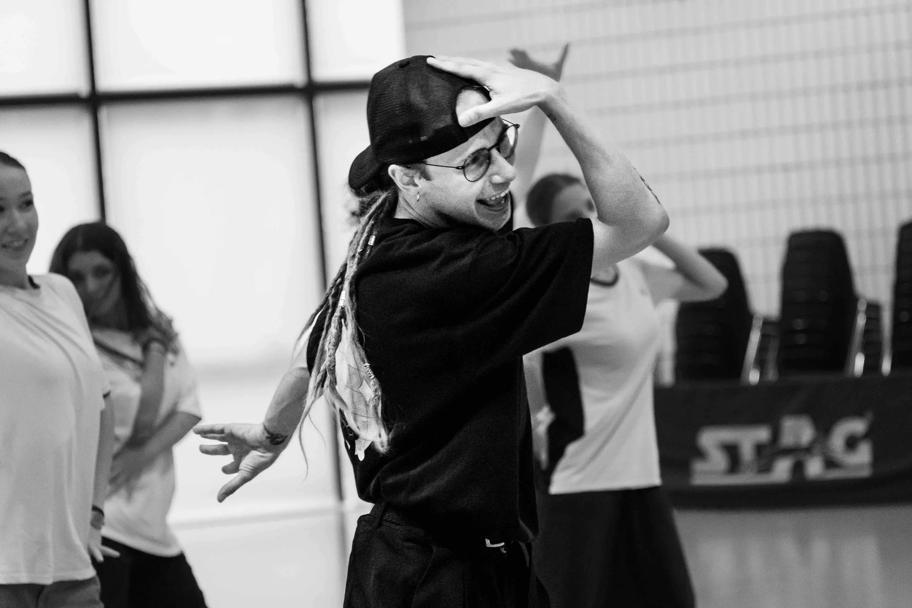 A teacher in a cap and glasses dances among the students