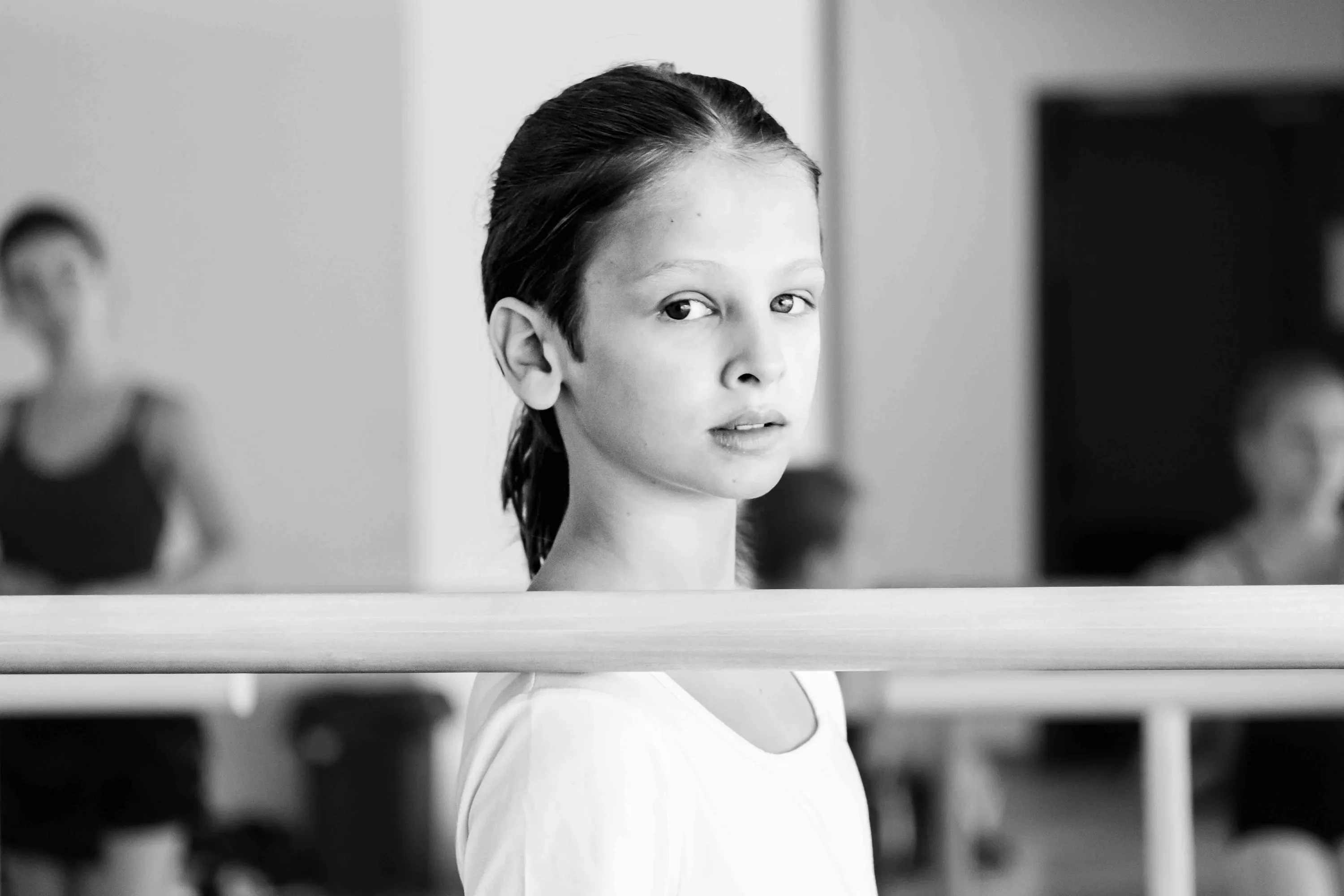A young student looks into the camera from behind the barre