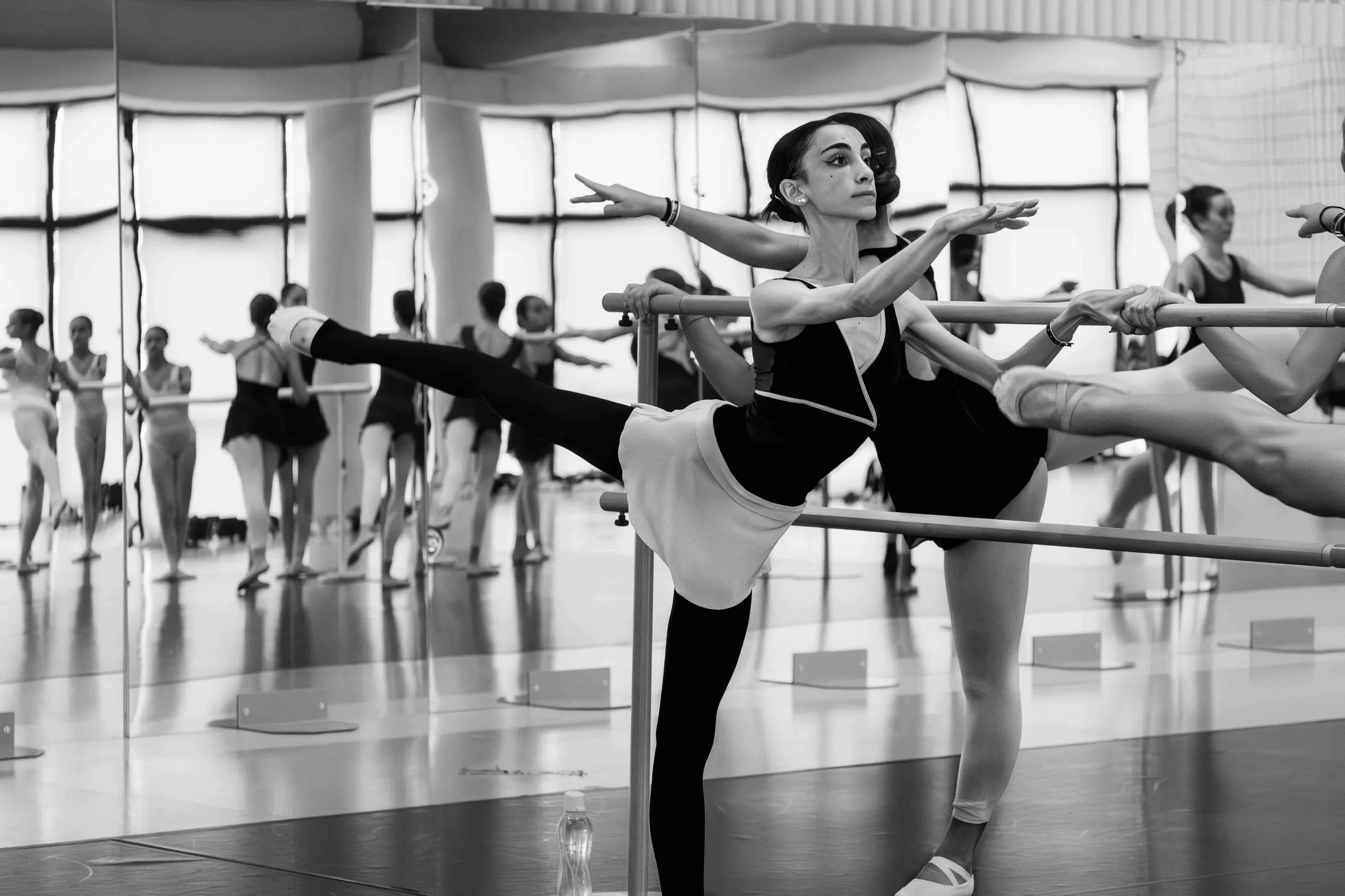 Students at the barre with legs raised before the mirror