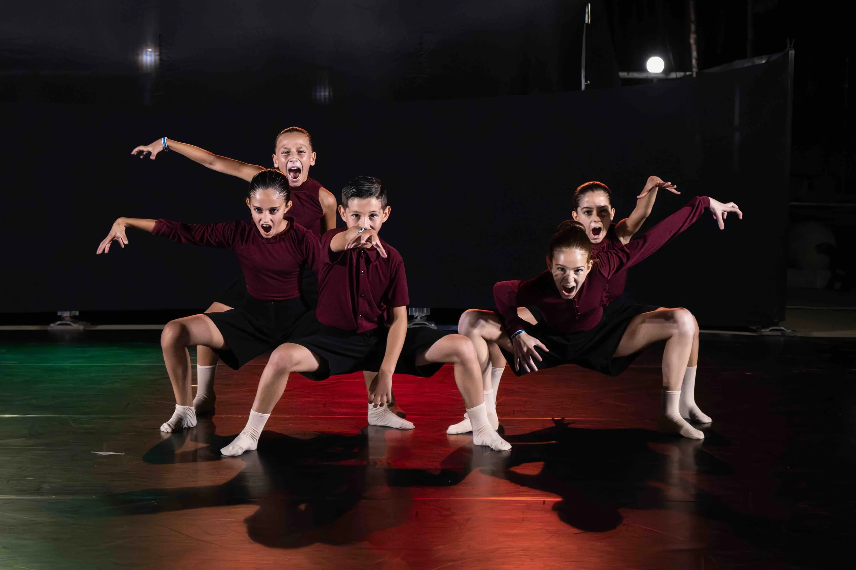 A group of young dancers in red crouching on the floor