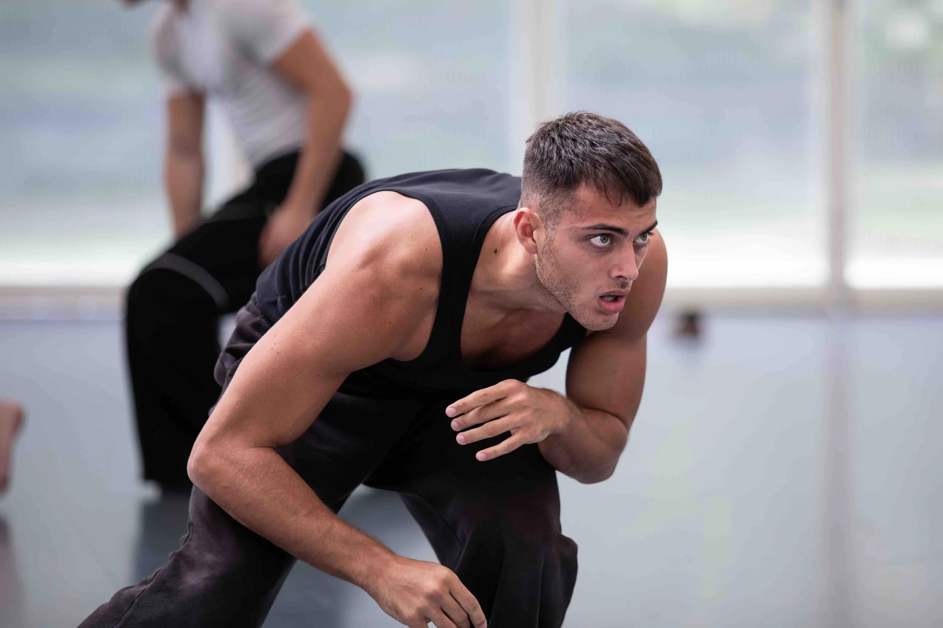 A dancer in a black vest bending forward, focused