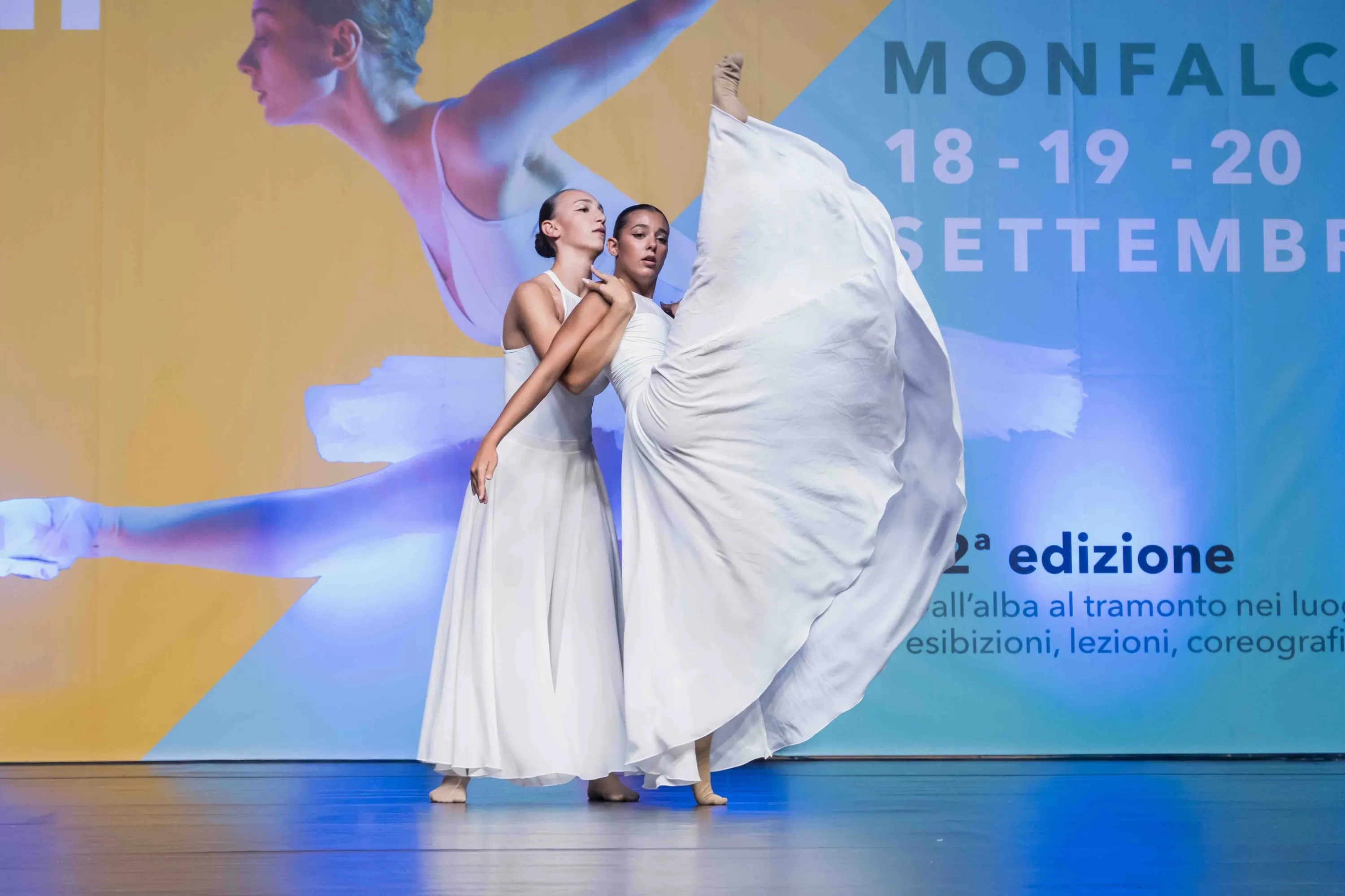 Two dancers in white dresses, one skirt lifted like a wing