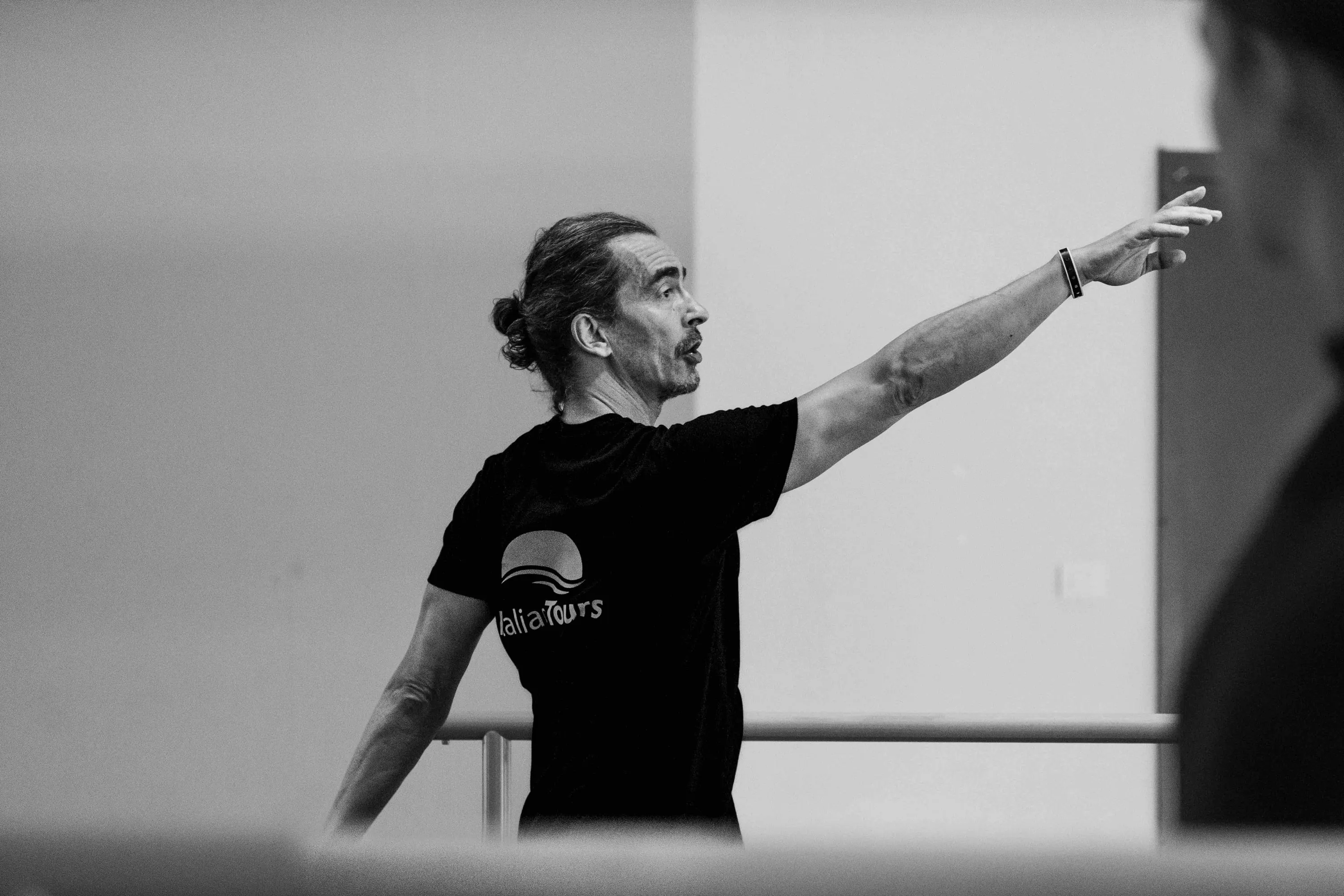 The teacher points with an outstretched arm near the barre