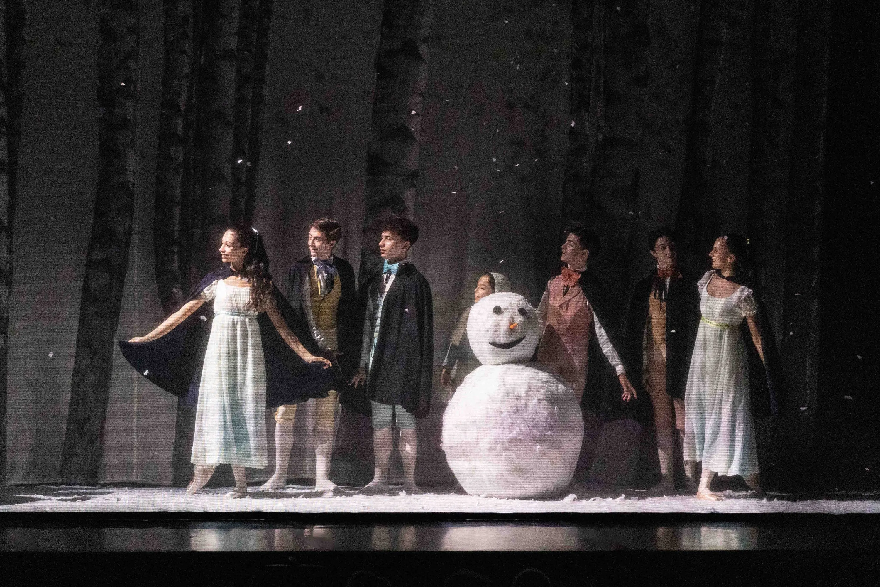 A snowy scene with a snowman and young performers in costume