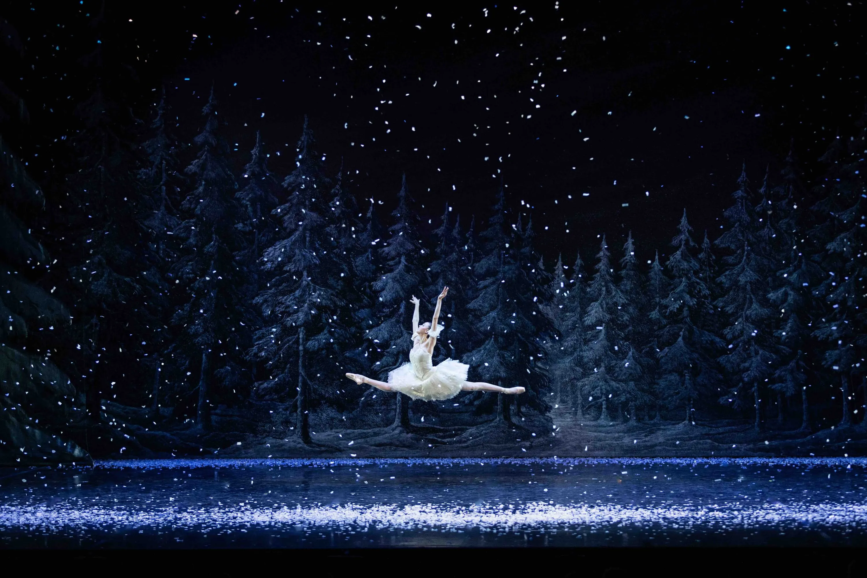 A ballerina leaping in the forest as snow falls