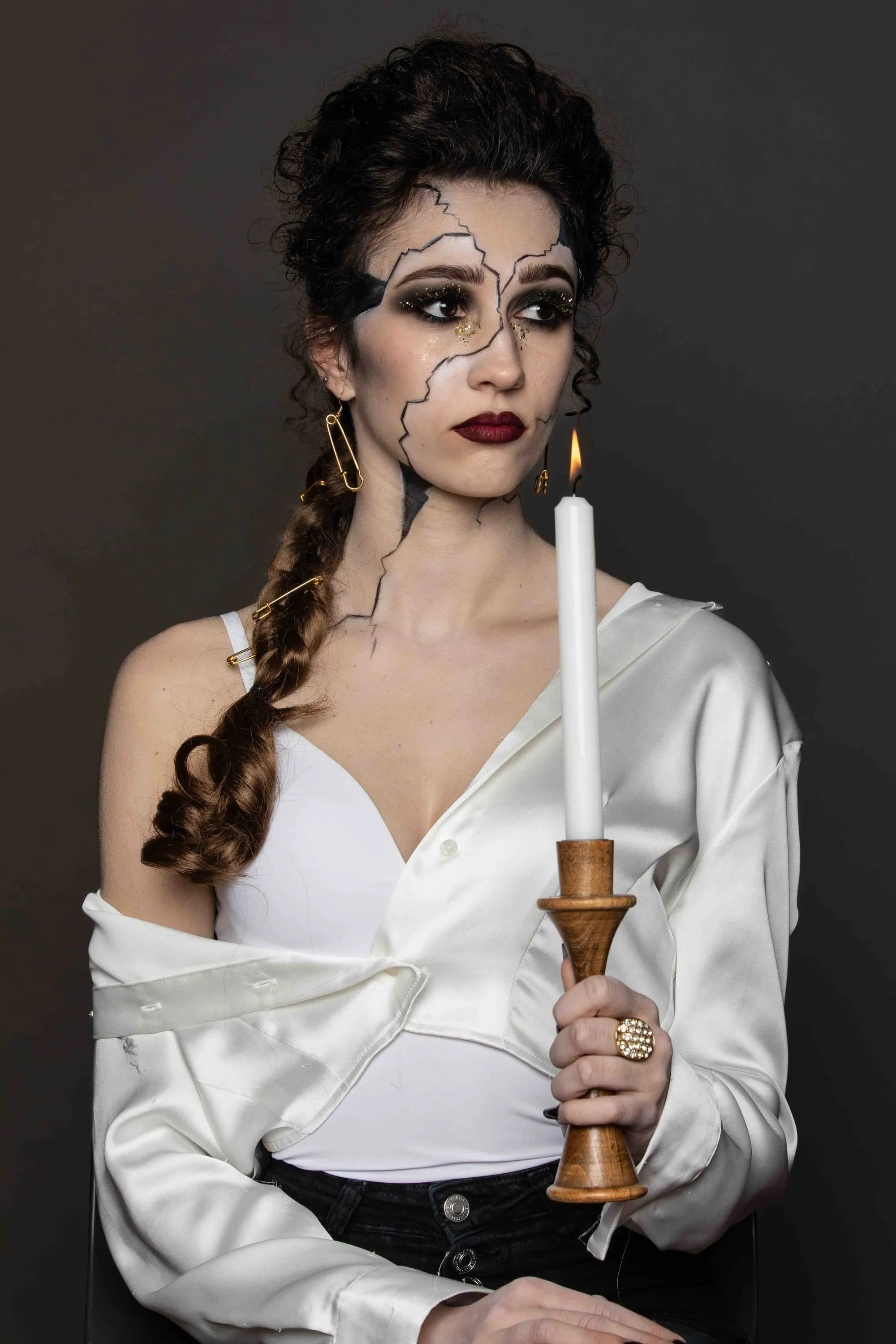 Theatrical make-up with cracks on the face, the model holds a candle