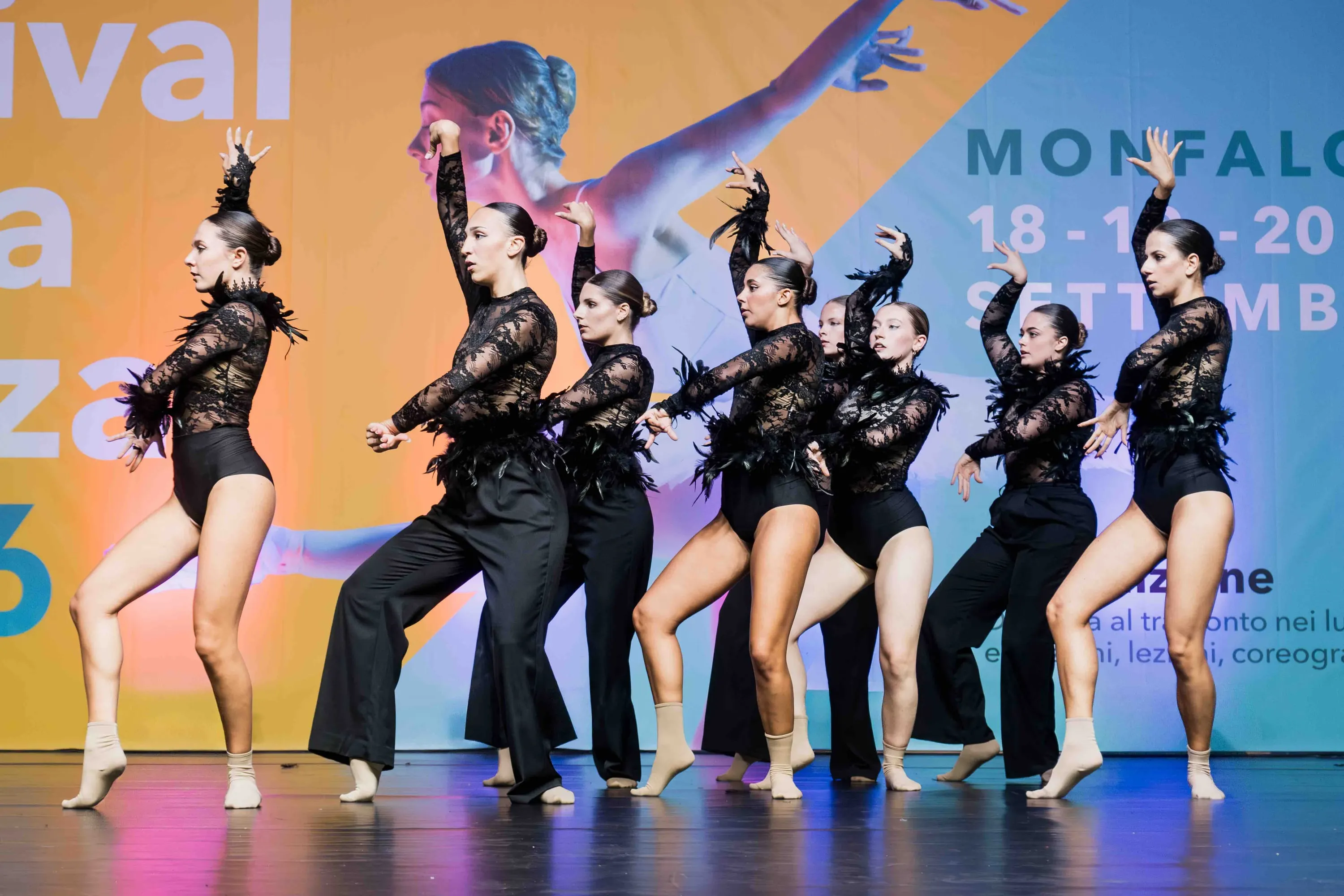 A group of dancers in black with feathers, in a bold pose