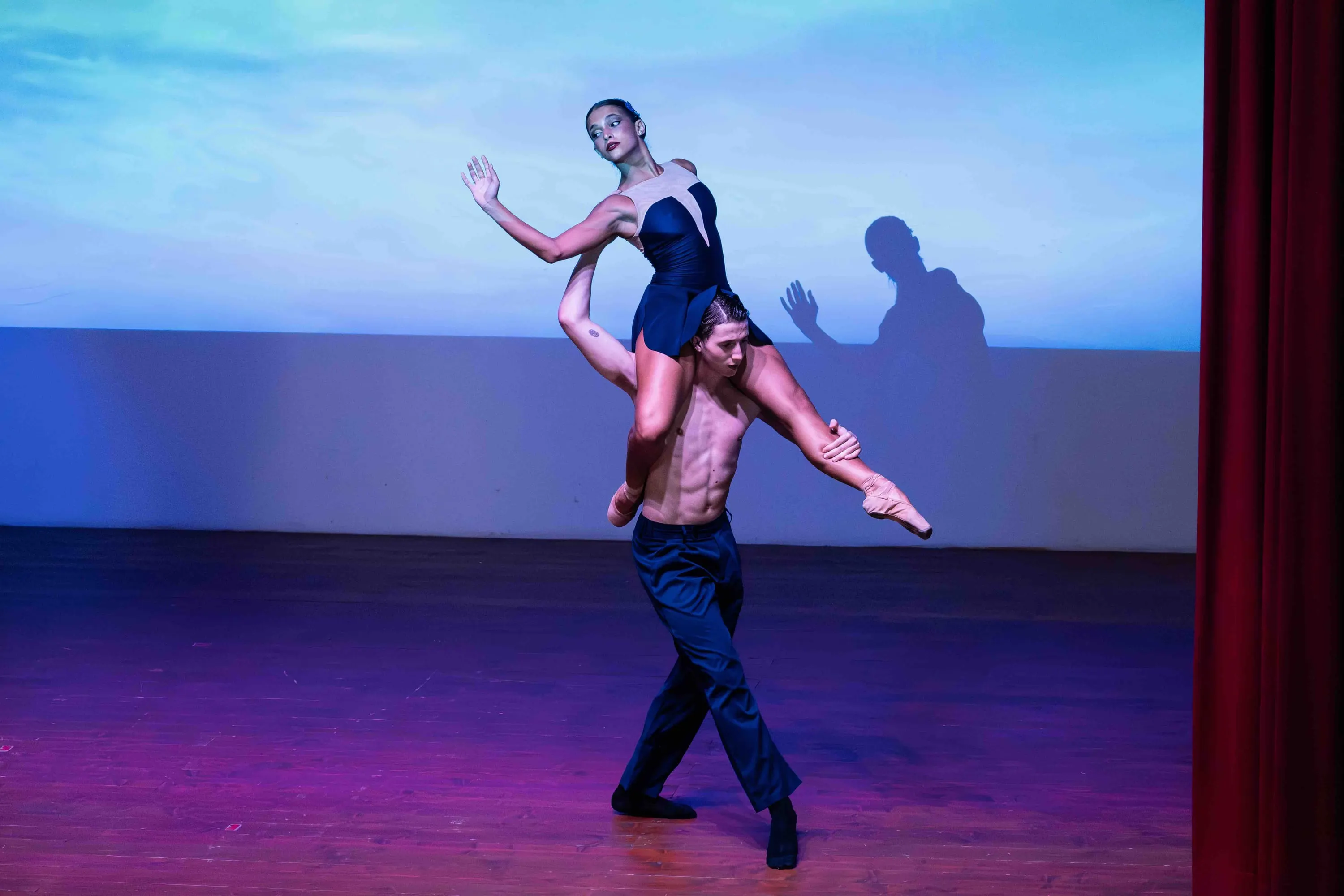 A dancer carries a ballerina on his shoulders, in blue light