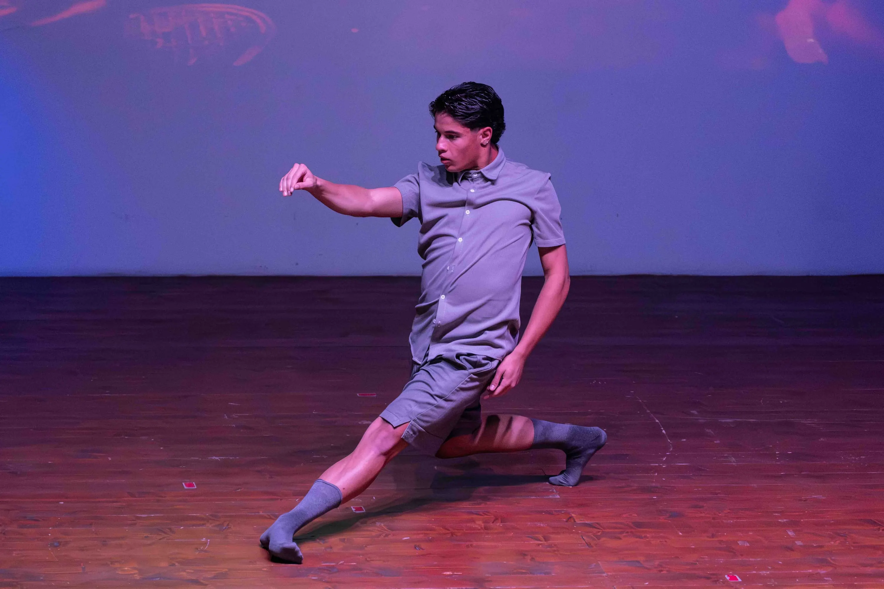 A young dancer in a deep lunge on stage, in violet light