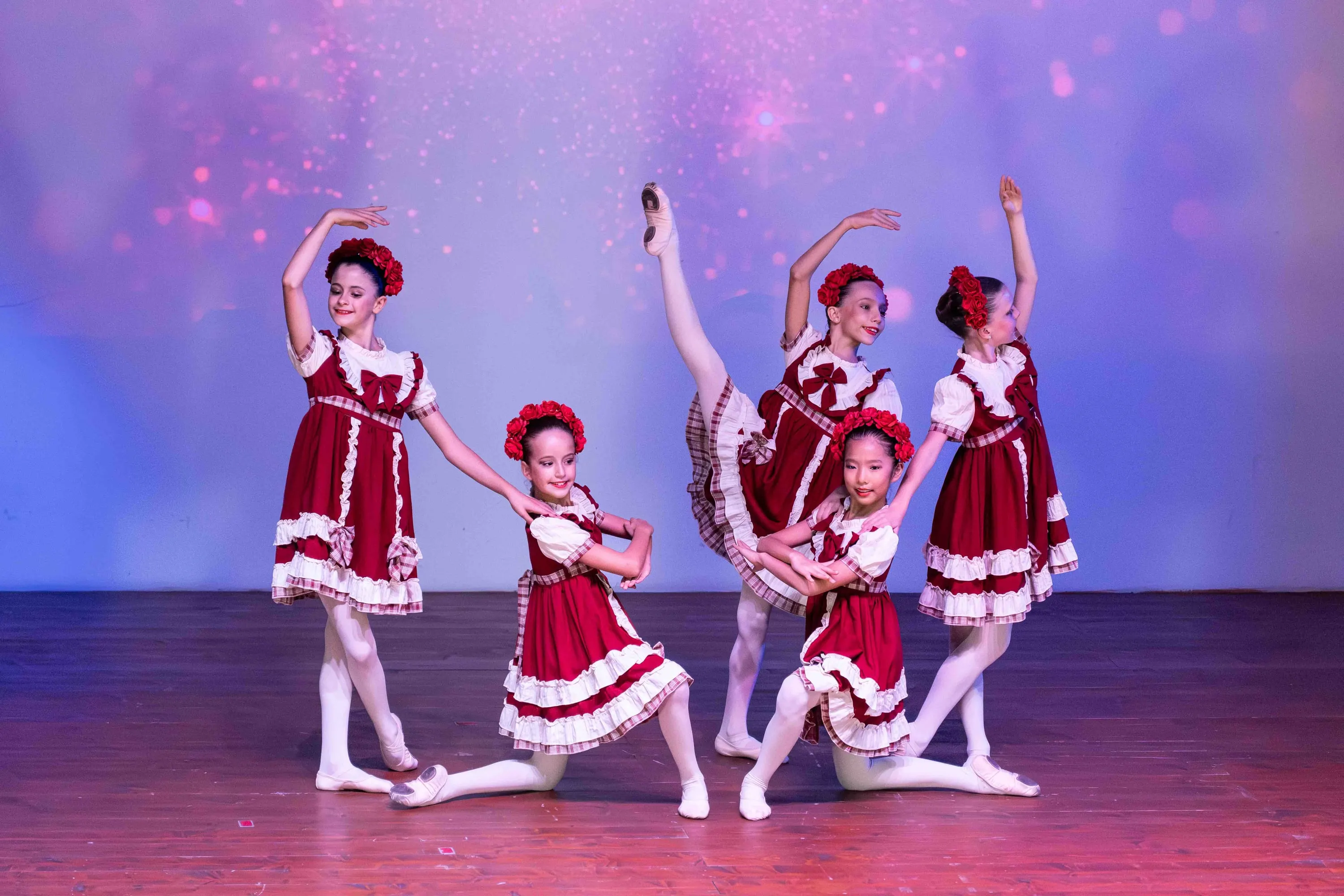 A group of young girls in red costumes posing on stage