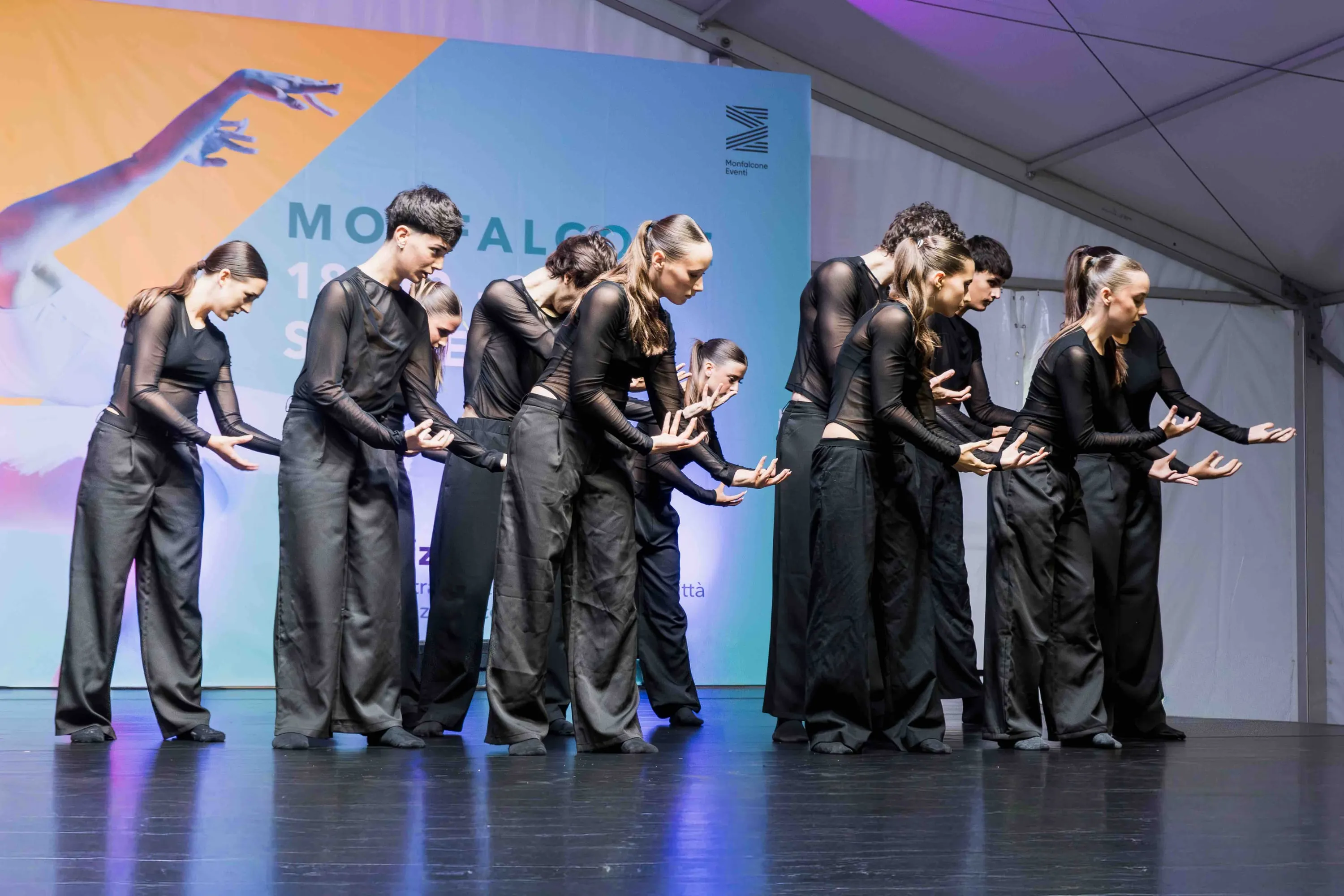 A line of dancers in black reaching their arms forward