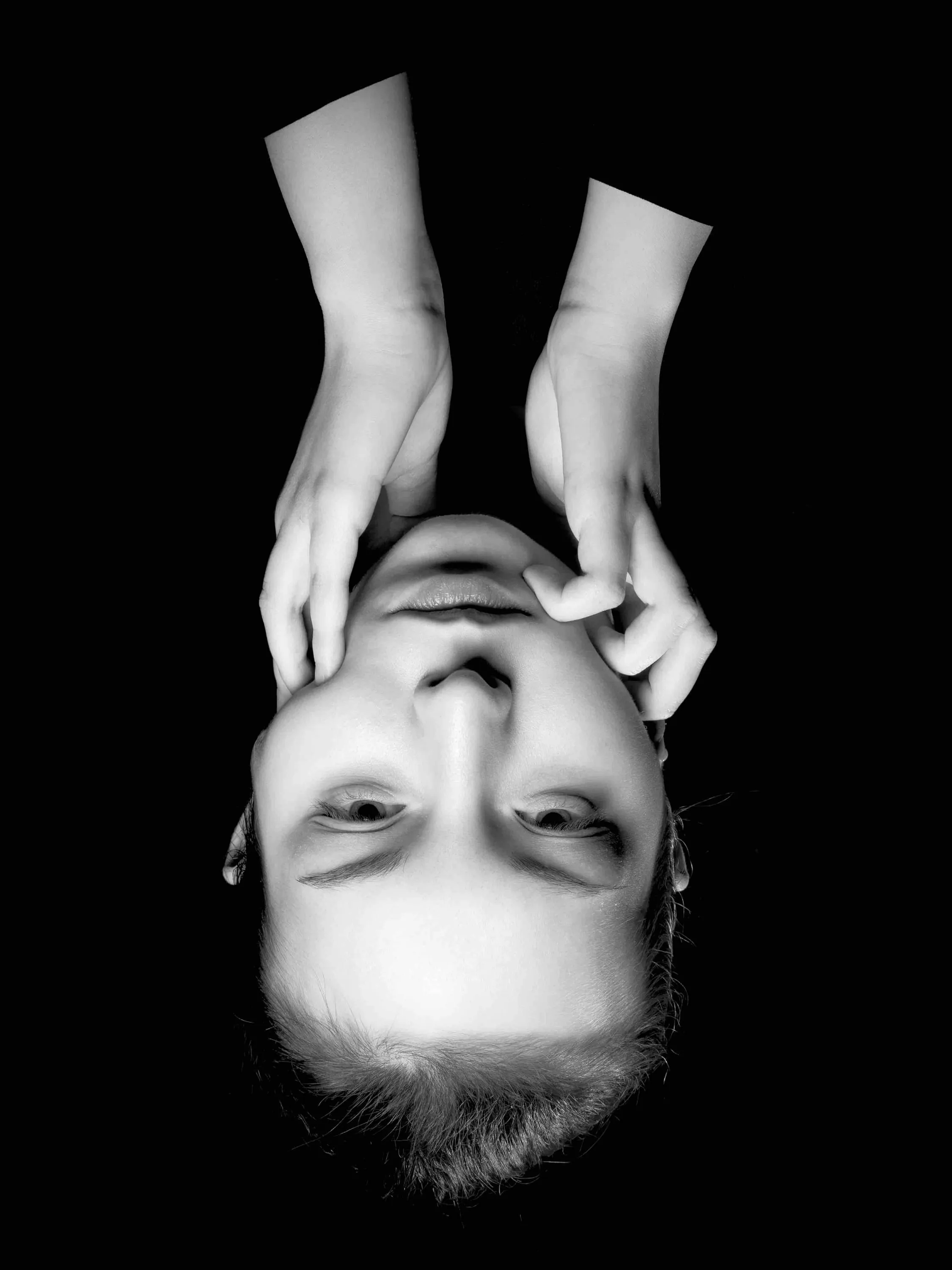 An upside-down black-and-white portrait, hands framing the face