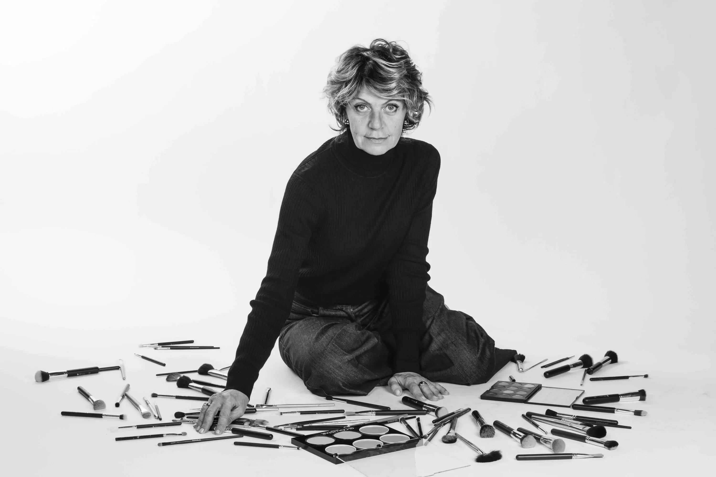A make-up artist seated on the floor surrounded by brushes and palettes