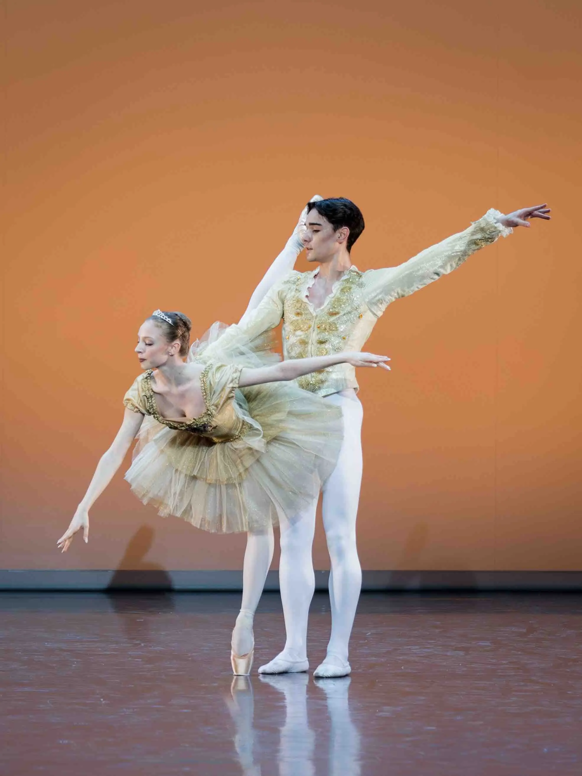 A classical pas de deux in pale costumes against an orange backdrop