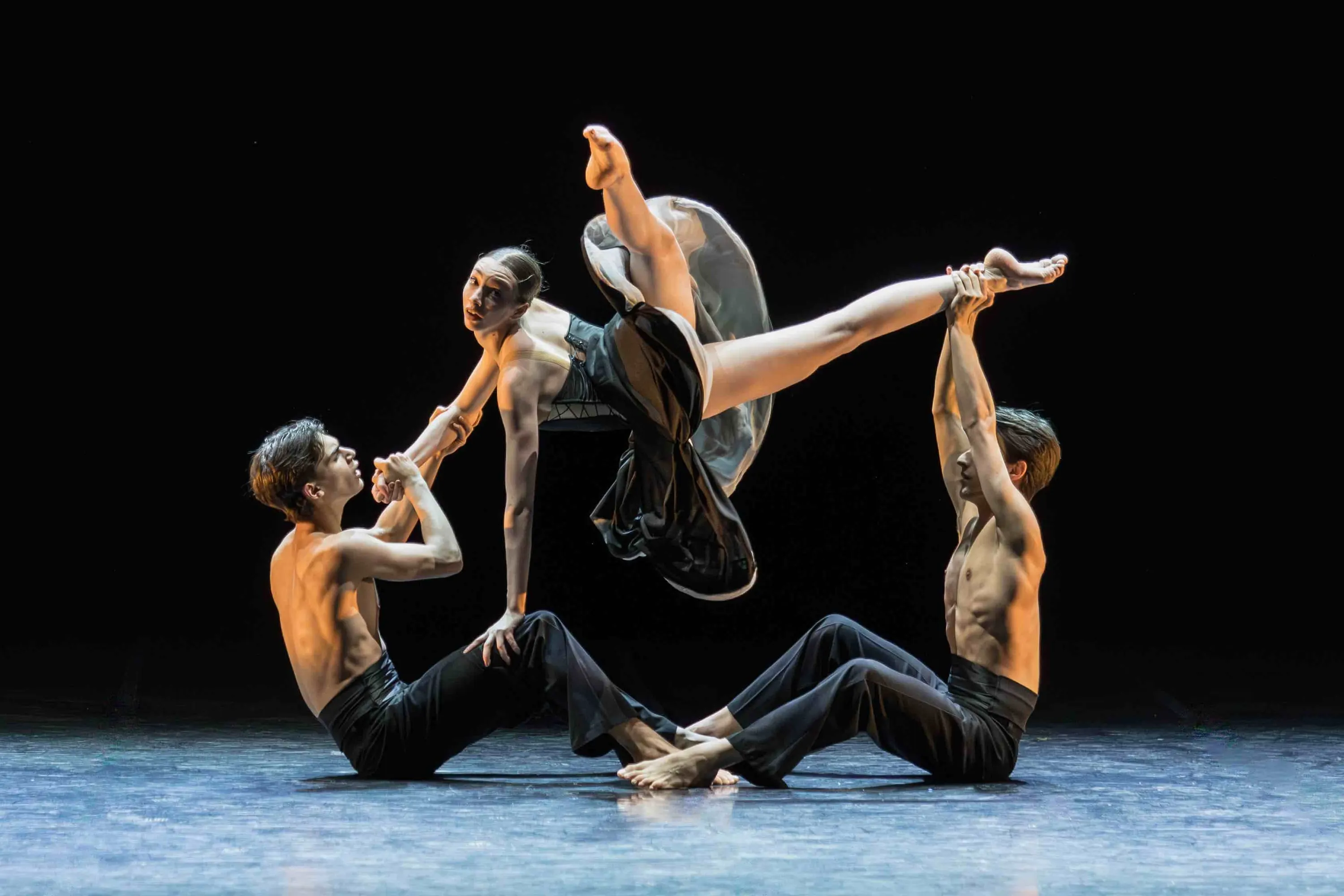 Three dancers lift a ballerina into the air, black background