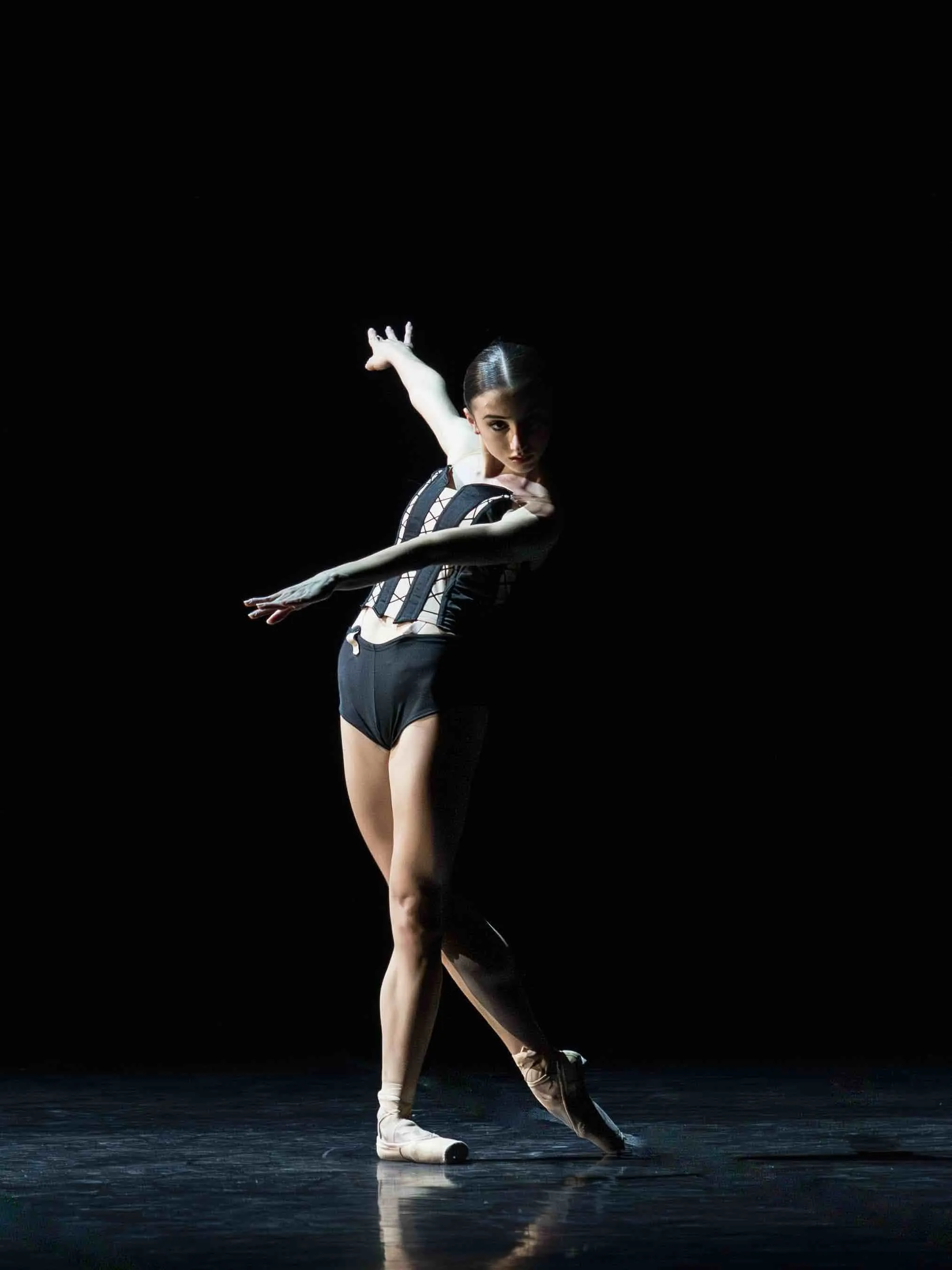 A dancer in a striped leotard balancing en pointe against a black background