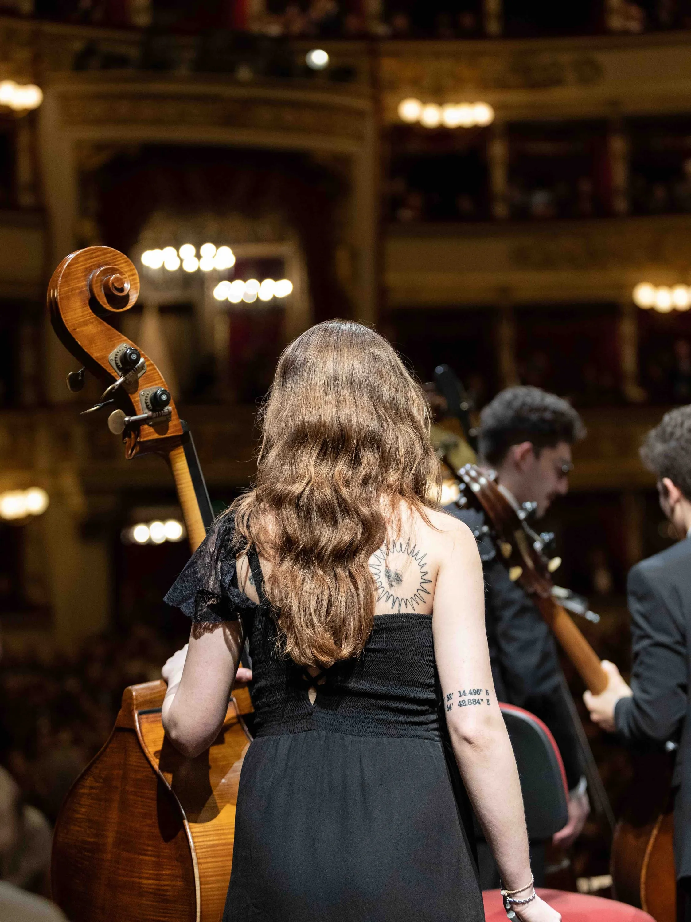 A double bass player from behind, with La Scala's boxes beyond