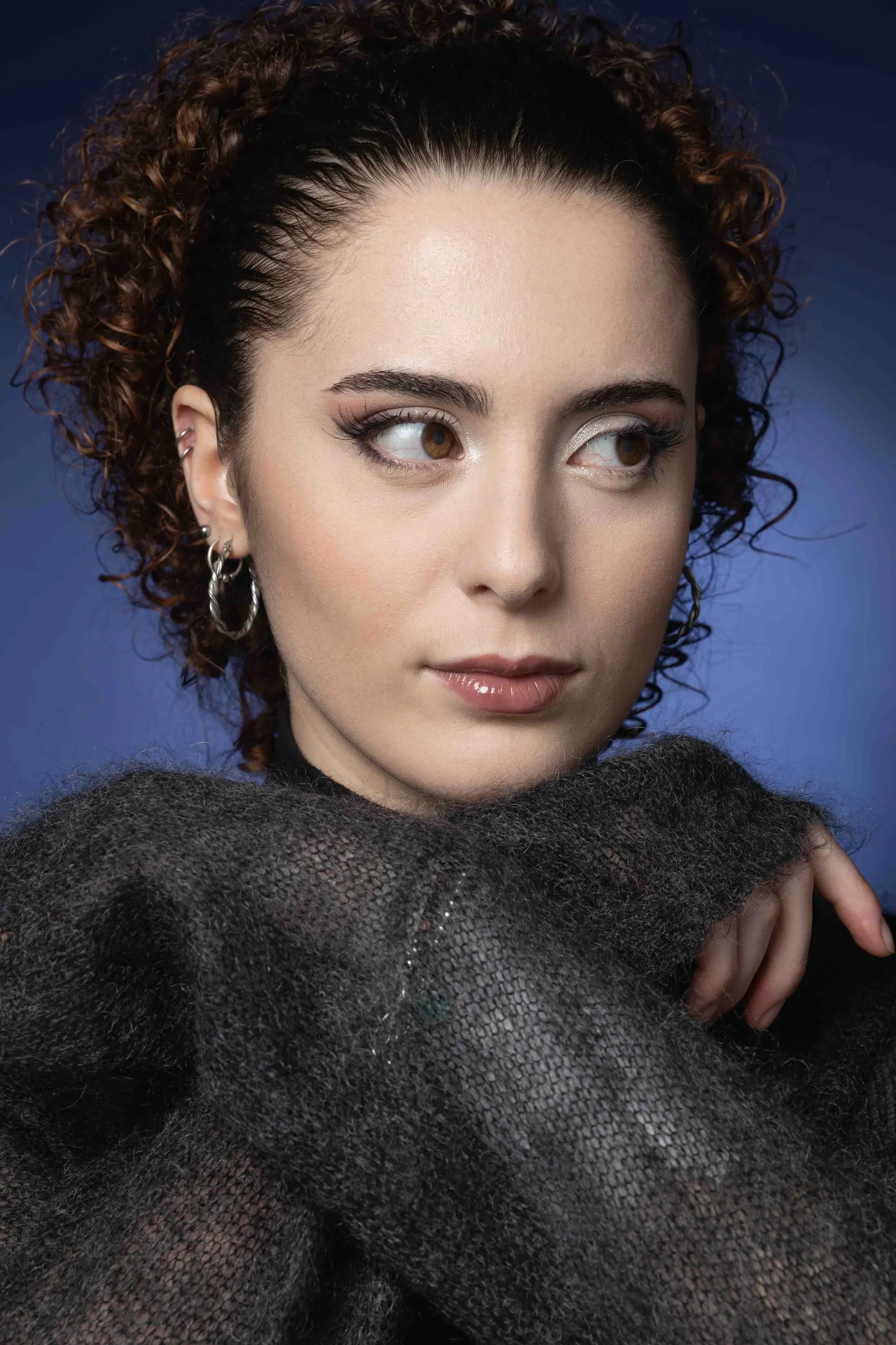 Portrait of a curly-haired young woman against blue, glancing aside